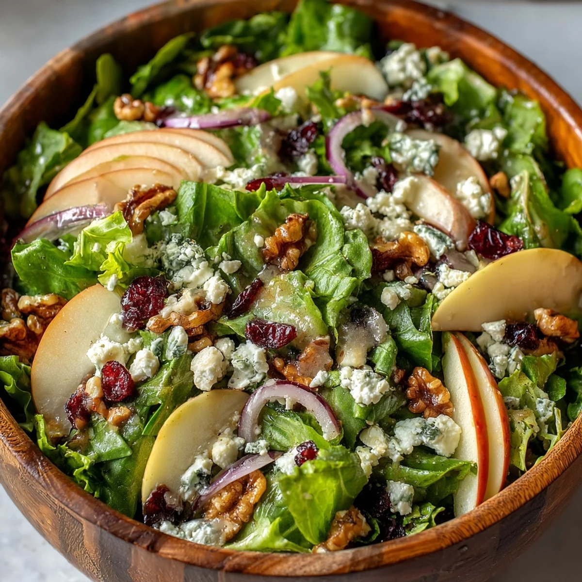 Close-up of Mixed Greens and Apple Bowl featuring vibrant greens, crumbled cheese, and chopped walnuts on a rustic table.