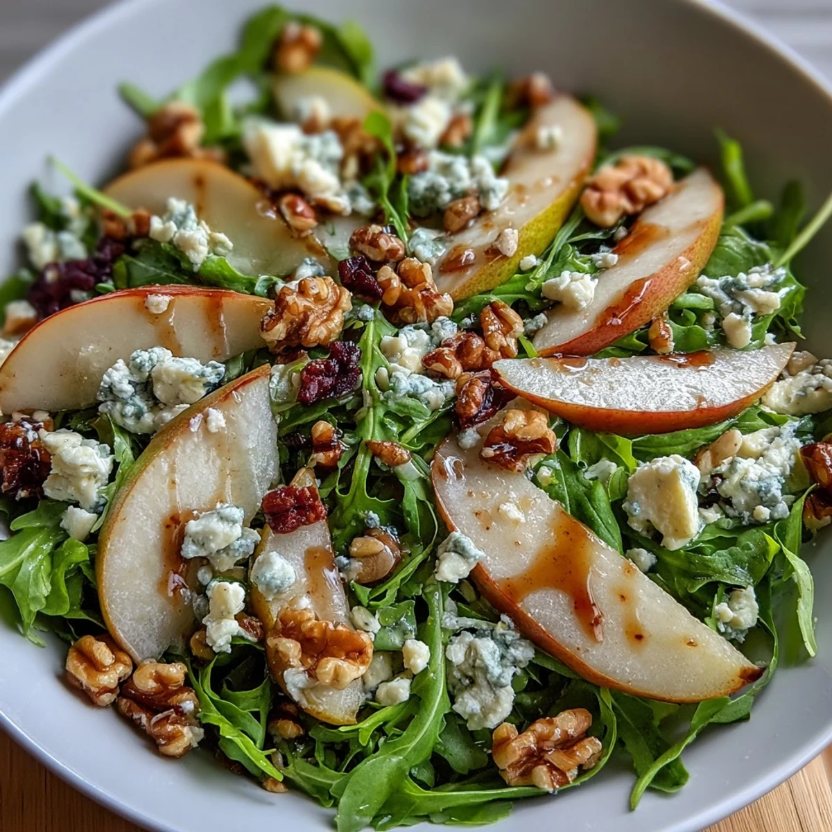 Close-up of an Arugula and Pear Bowl highlighting glistening olive oil, honey, and crumbled goat cheese on fresh greens.