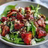 Spring Dinner Party Strawberry Arugula Salad with Balsamic Glaze on a white plate with strawberries, arugula, goat cheese, and nuts.
