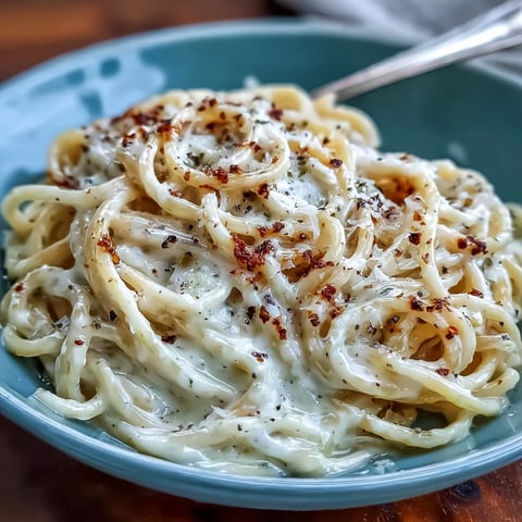 Steaming spaghetti tossed in a skillet with freshly cracked black pepper and Pecorino Romano to create Cacio e Pepe.