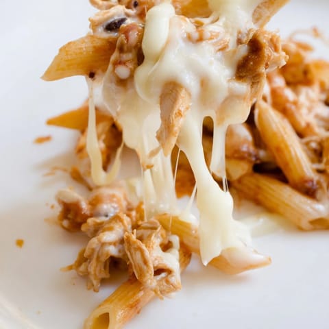 A serving spoon scoops creamy Chicken Enchilada Pasta with black beans, revealing saucy pasta and shredded chicken inside.