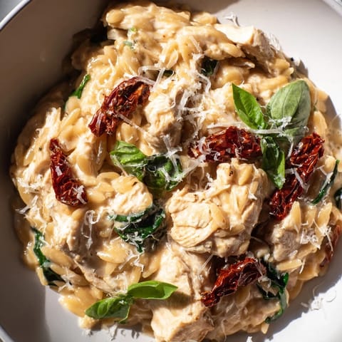Tuscan Chicken Orzo sizzling in a deep skillet, blending golden chicken pieces with vibrant red tomatoes and herbs.