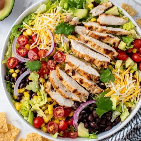 A vibrant bowl of honey lime chicken taco salad garnished with cherry tomatoes, red onion, and crunchy tortilla strips.  