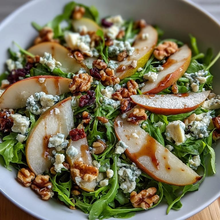 Close-up of an Arugula and Pear Bowl highlighting glistening olive oil, honey, and crumbled goat cheese on fresh greens.
